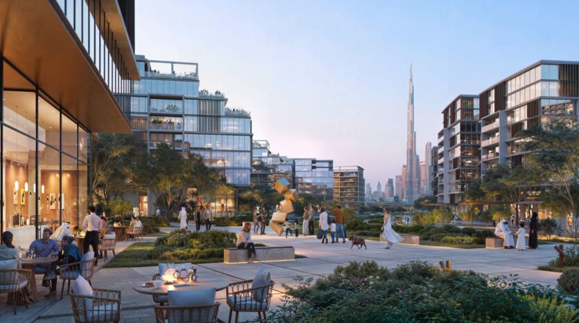 Люди отдыхают и встречаются на современной открытой площадке в The Residences DIFC, окруженной стеклянными зданиями, зеленью и художественными скульптурами, с видом на Бурж-Халифа, виднеющийся на горизонте на закате солнца.