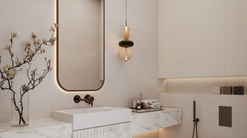 Современная ванная комната в The Residences DIFC включает мраморную столешницу, прямоугольную раковину, настенный смеситель, овальное зеркало с подсветкой, подвесные светильники и декоративные ветки в вазе. Туалетные принадлежности и полотенца аккуратно разложены на столешнице.