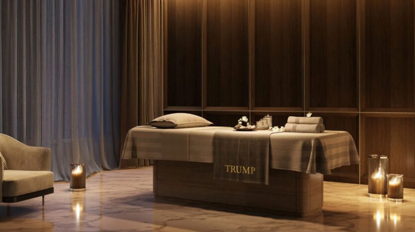 La luxueuse salle de spa du Trump Plaza comprend une table de massage drapée de linge beige portant l'inscription "TRUMP", entourée de bougies, de serviettes et d'un décor élégant, avec un éclairage doux et des sols en marbre créant une ambiance paisible.