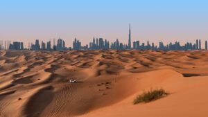 Ein weißer SUV fährt über Sanddünen mit sichtbaren Reifenspuren, vor dem Hintergrund der Skyline der modernen Stadt Dubai und dem Burj Khalifa-Turm unter klarem Himmel. Das Bild fängt das Leben in Dubai inmitten der sich durch die globale Erwärmung verändernden Landschaft ein.