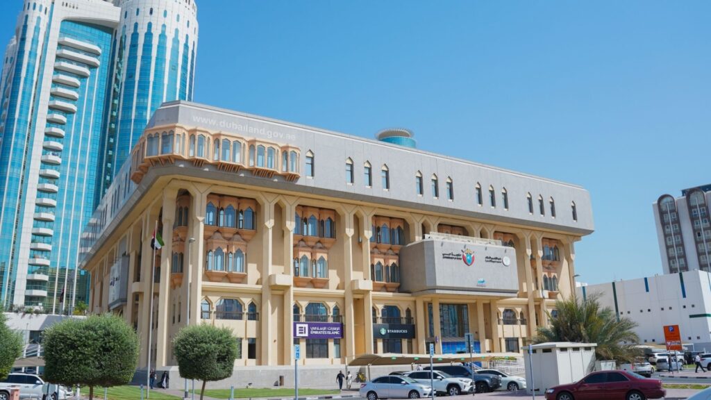 Ein großes Regierungsgebäude mit Bogenfenstern und dekorativen Säulen erhebt sich unter einem strahlend blauen Himmel, umgeben von modernen Wolkenkratzern, die die Dynamik des Immobilienmarktes in Dubai widerspiegeln, Palmen, geparkten Autos und Menschen, die in der Nähe spazieren gehen.