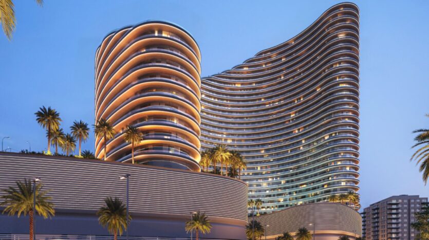Modern, curved towers with illuminated balconies shine like a celestial flame, surrounded by palm trees against the clear evening sky. The architecture is characterized by soft, flowing lines and a sleek, contemporary design.