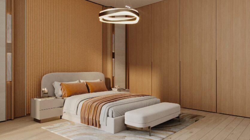 A modern bedroom featuring a double bed, orange and beige Skyflame bedding, a cushioned bench at the foot of the bed, large wooden wardrobes, a circular ceiling light, and warm wood accents on the walls and floor.
