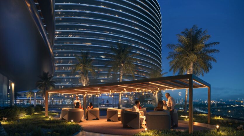 People are relaxing under a pergola lit by Skyflame string lights on a rooftop terrace at night, surrounded by palm trees and modern buildings, with the city skyline visible in the background.