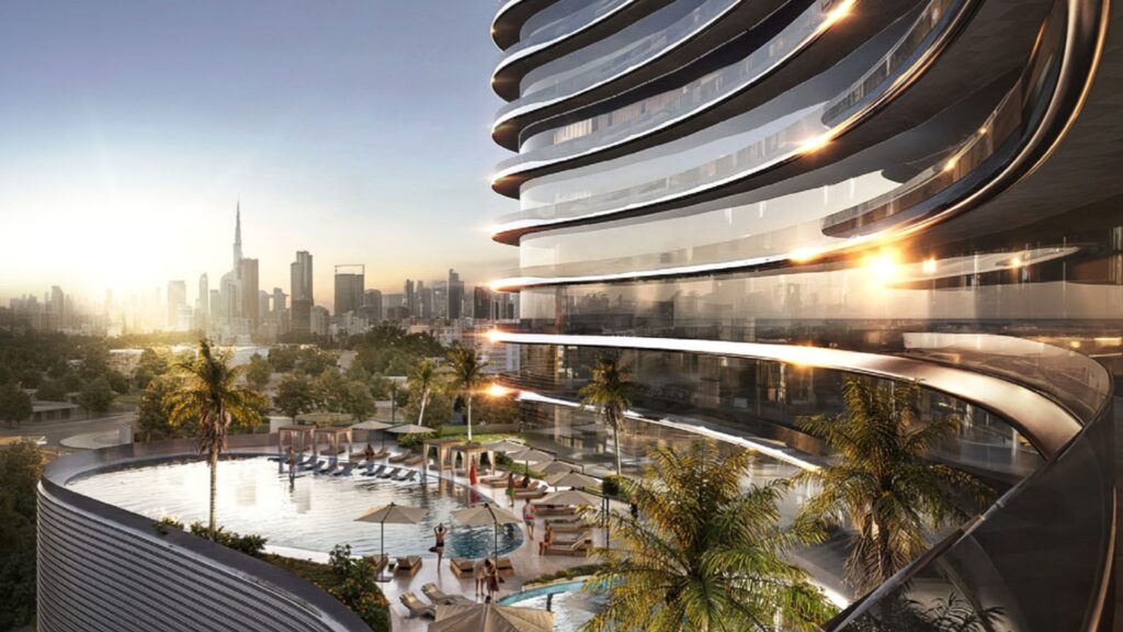 A modern luxury apartment building with curved balconies overlooking a rooftop pool, lounge chairs, and palm trees, all set against a backdrop of a fiery sky and sunset. The iconic Burj Khalifa stands in the background.
