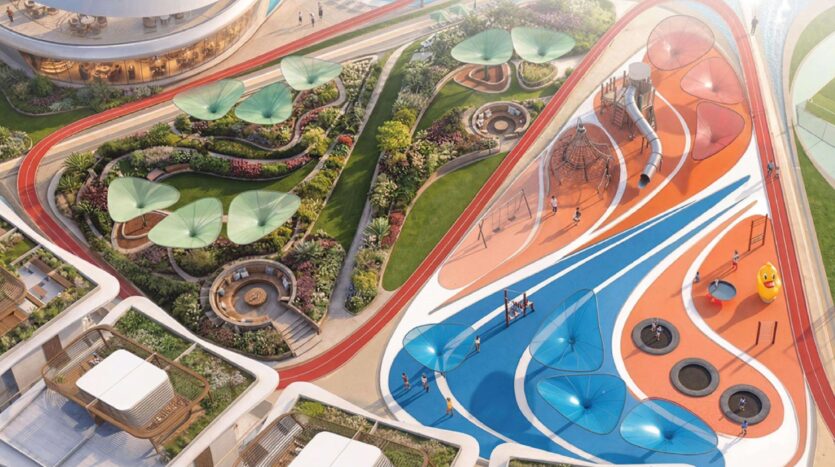 Luftaufnahme eines modernen Spielplatzes in Greenz by Danube mit farbenfrohen Flächen in Blau und Orange, Klettergerüsten, Schaukeln und schattigen Sitzgelegenheiten neben landschaftlich gestalteten Gärten und gewundenen Spazierwegen.
