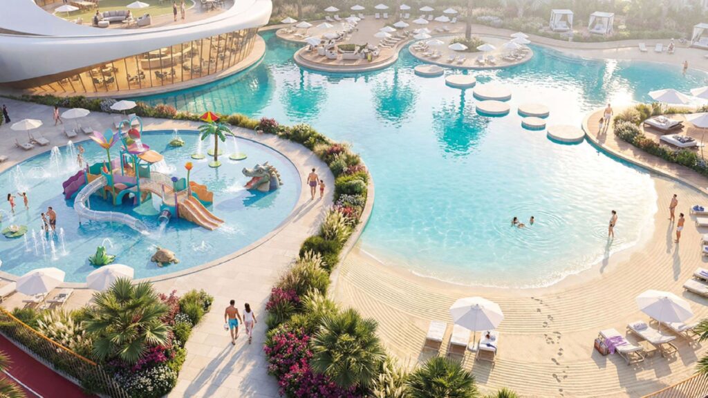 Luftaufnahme des Pools des Greenz by Danube-Komplexes mit einem Sandstrand am Eingang, Liegestühlen, Sonnenschirmen und einem bunten Kinderspielplatz. Mehrere Personen baden und entspannen sich, umgeben von üppigen Pflanzen und Gärten.