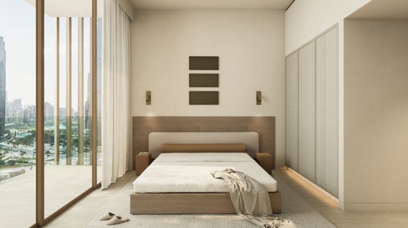 Minimalist bedroom with a large window, beige walls, a JAD288 wooden bed with white sheets, two bedside tables, and three rectangular wall art pieces above the bed. A throw blanket and slippers are placed on the floor near the bed.