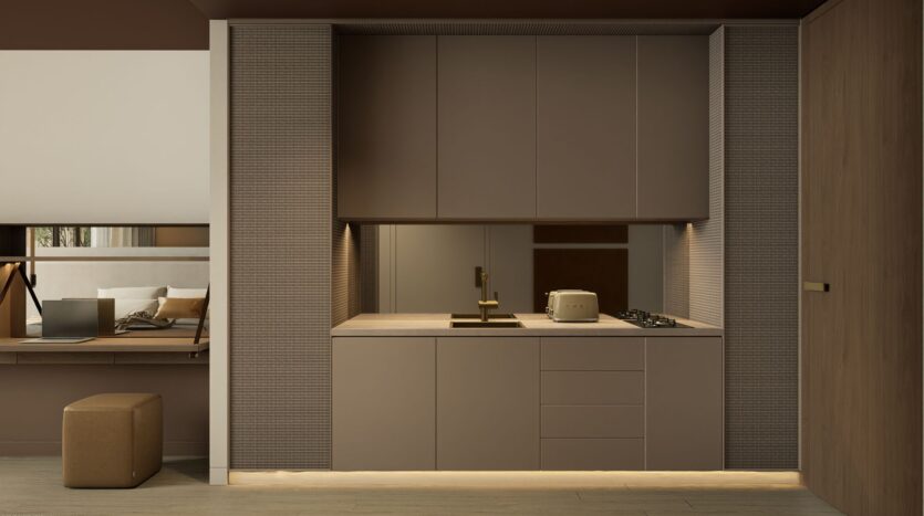 A modern, minimalist kitchen with matte taupe cabinets, a built-in sink, stove, toaster, and under-cabinet lighting. Model JAD288 features a comfortable workspace with a laptop and stool visible on the left.
