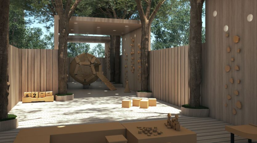 The modern outdoor playground JAD288 features wooden walls and floors, trees growing in the space, climbing holds on the walls, wooden blocks and shapes, and a large geometric climbing structure with a slide. Sunlight filters through the trees.
