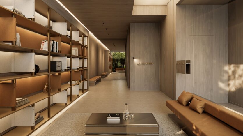 A modern, minimalist living room with beige walls, a long brown sofa, a metal coffee table, and open shelves with books and decorative items. Through the hallway at the back, JAD288 offers breathtaking views of the greenery.