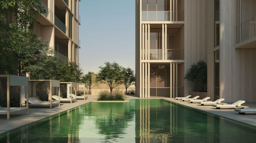 A modern outdoor pool, labeled JAD288, is surrounded by lounge chairs, cabanas, and large contemporary buildings, with green trees providing shade and reflections sparkling in the calm water.