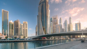 Eine moderne Uferpromenade in Dubai mit hohen Wolkenkratzern, einer geschwungenen Fußgängerbrücke und einer gepflasterten Promenade mit Geländern entlang eines ruhigen Kanals – ein Gebiet, das weiterhin Investoren auf den dynamischen Immobilienmarkt in Dubai lockt.