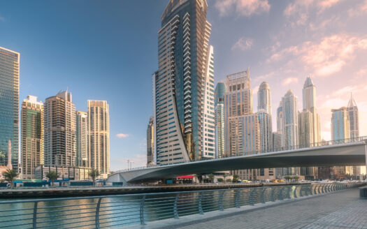 Un front de mer moderne à Dubaï avec de hauts gratte-ciel, un pont piétonnier incurvé et une promenade pavée bordée de garde-corps le long d'un canal calme - une zone qui continue d'attirer les investisseurs sur le dynamique marché immobilier à Dubaï.