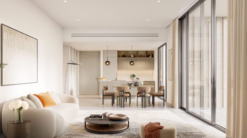 Salon et salle à manger minimalistes et modernes au Tara Park avec des tons neutres, un canapé rond beige, une table basse, une table à manger pour six personnes, des lampes suspendues, de grandes fenêtres et une cuisine ouverte en arrière-plan.