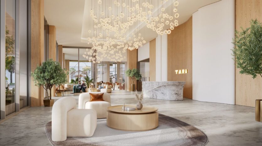 Hall d'entrée moderne de l'hôtel Tara Park avec de grandes fenêtres, un mobilier aux tons neutres, un bureau de réception en marbre, des plantes et un élégant luminaire au plafond avec des orbes en verre suspendus. La lumière naturelle remplit l'intérieur spacieux et élégant.