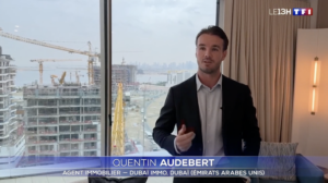 Ein Mann im Anzug steht vor einem Fenster, hinter dem Kräne und Gebäude zu sehen sind, während ein Text auf dem Bildschirm ihn als Quentin Audebert von Dubaï Immo vorstellt; dies wird in einem Nachrichtenbeitrag von TF1 gezeigt.