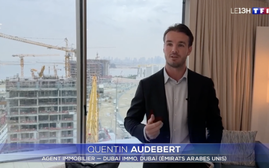 A man in a suit stands in front of a window with cranes and buildings visible in the background, while on-screen text identifies him as Quentin Audebert of Dubai Immo, featured in a news segment on TF1.