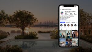 Auf einem Smartphone ist das Instagram-Profil von „Dubai Immo“, einer führenden Immobilienagentur, zu sehen: am Rande eines luxuriösen Pools bei Sonnenuntergang, im Hintergrund die Skyline der Stadt und atemberaubende Palmen.