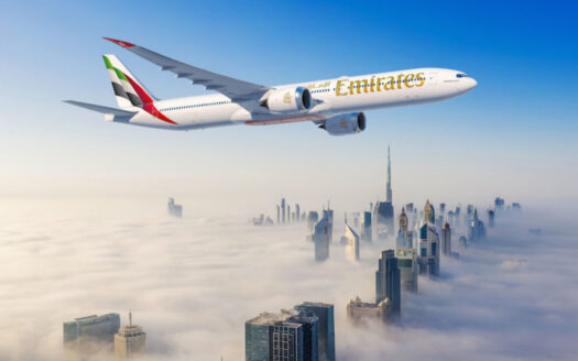 Un avion d'Emirates survole un paysage urbain couvert de brouillard, avec des gratte-ciel emblématiques comme Burj Khalifa émergeant de la brume, illustrant la sécurité que Dubaï offre à ceux qui souhaitent voyager à Dubaï sous un ciel bleu clair.
