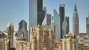 Blick auf die Skyline mit beigefarbenen, verzierten Wohngebäuden im Vordergrund und modernen Glaswolkenkratzern im Hintergrund unter strahlend blauem Himmel, die die Widerstandsfähigkeit Dubais inmitten der Immobilienkrise und globaler Spannungen wie dem Krieg im Iran widerspiegeln.
