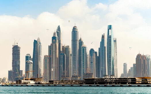 Une vue panoramique de la ligne d'horizon d'une ville moderne avec de nombreux gratte-ciel le long d'un front de mer, certains en construction, dans un ciel partiellement nuageux - une scène inspirante qui incite de nombreuses personnes à investir à Dubaï.