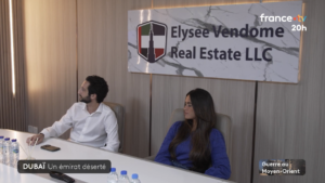 Zwei Personen sitzen an einem Konferenztisch mit Wasserflaschen vor einer Tafel mit der Aufschrift „Elysee Vendome Real Estate LLC“. Im Bild ist ein Einblendung des französischen Fernsehsenders zu sehen, die lautet: „Dubai-Immobilien in den 20-Uhr-Nachrichten von France 2“, wobei Dubai und der Nahe Osten am unteren Bildrand hervorgehoben sind.