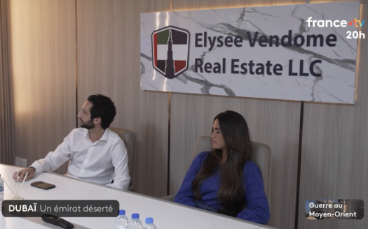 Zwei Personen sitzen an einem Konferenztisch mit Wasserflaschen vor einer Tafel mit der Aufschrift „Elysee Vendome Real Estate LLC“. Im Bild ist ein Einblendung des französischen Fernsehsenders zu sehen, die lautet: „Dubai-Immobilien in den 20-Uhr-Nachrichten von France 2“, wobei Dubai und der Nahe Osten am unteren Bildrand hervorgehoben sind.