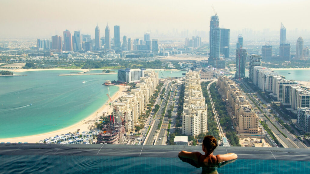 Una persona si rilassa in una piscina a sfioro affacciata sulla linea dell'orizzonte e sulle spiagge di Dubai. La vista mozzafiato mette in evidenza il contrasto tra il modo in cui gli abitanti di Dubai vivono la crisi legata alla guerra in Iran, tra lusso urbano e incertezza regionale.