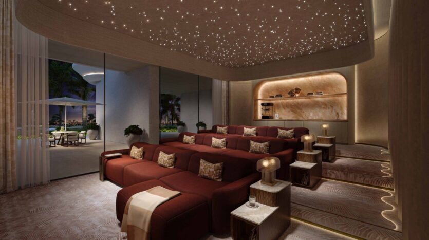 La lujosa sala de cine de las residencias Amali cuenta con butacas rojas dispuestas en gradas, mesitas auxiliares con lámparas y un techo estrellado. Los ventanales que van del suelo al techo dan a un patio adornado con palmeras y elegantes muebles de exterior.