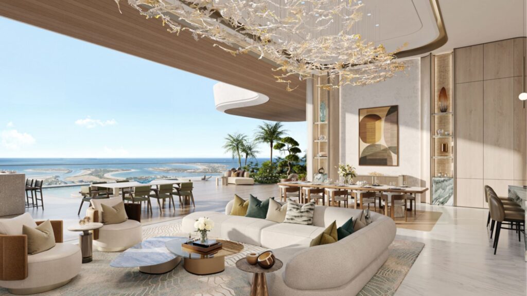 El lujoso salón-comedor diáfano de las residencias Amali, con una decoración moderna, una gran lámpara de araña de estilo abstracto, ventanas de suelo a techo con vistas al océano, mobiliario contemporáneo, plantas de interior y tonos neutros en todo este espacioso y luminoso interior.