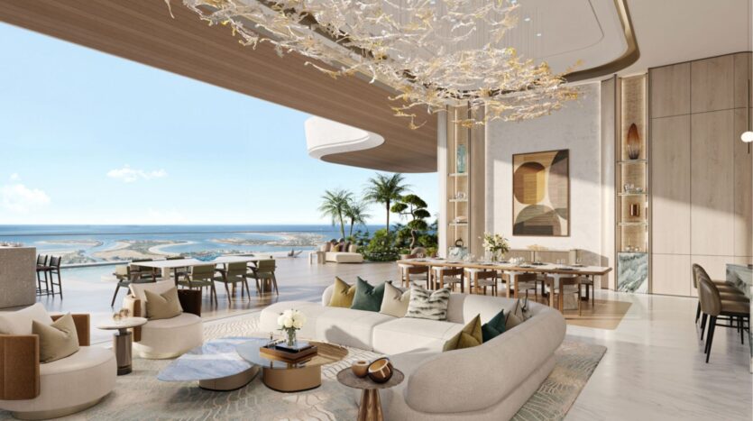 El lujoso salón-comedor diáfano de las residencias Amali, con una decoración moderna, una gran lámpara de araña de estilo abstracto, ventanas de suelo a techo con vistas al océano, mobiliario contemporáneo, plantas de interior y tonos neutros en todo este espacioso y luminoso interior.