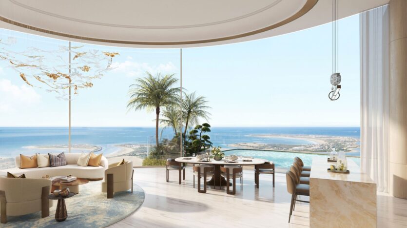 El amplio y moderno salón-comedor de las residencias Amali, con grandes ventanales curvos que van del suelo al techo y ofrecen unas vistas panorámicas del océano, el cielo azul, las palmeras y la costa de arena; mobiliario de tonos claros y decoración minimalista.