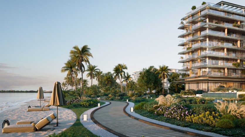 A wooden walkway winds through landscaped gardens next to the modern Cheval residences, with lounge chairs and umbrellas on a sandy beach beneath the palm trees at sunset.