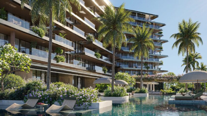 The modern, luxury Cheval Residences complex features numerous balconies, lush greenery, and palm trees. A crystal-clear blue pool with lounge chairs and umbrellas sits in the foreground under a clear, sunny sky.