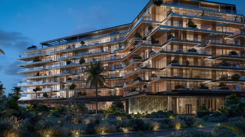 A modern, multi-story luxury apartment building, Les Résidences Cheval, is illuminated at dusk, featuring large floor-to-ceiling windows, spacious balconies, and lush landscaped gardens in the foreground. Palm trees and decorative lighting enhance the elegant atmosphere.
