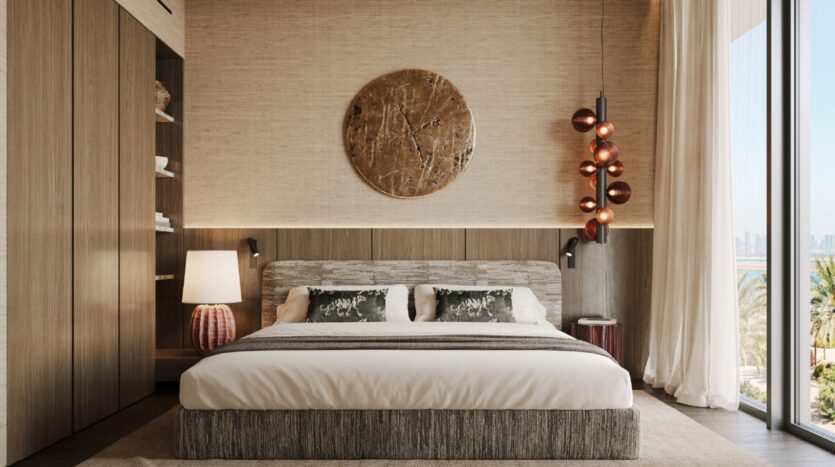 A modern bedroom at Cheval Residences featuring a king-size bed, two pillows, side tables with lamps, pendant lights, a floor-to-ceiling window with sheer curtains, wood paneling, and a round decorative wall art piece above the bed.