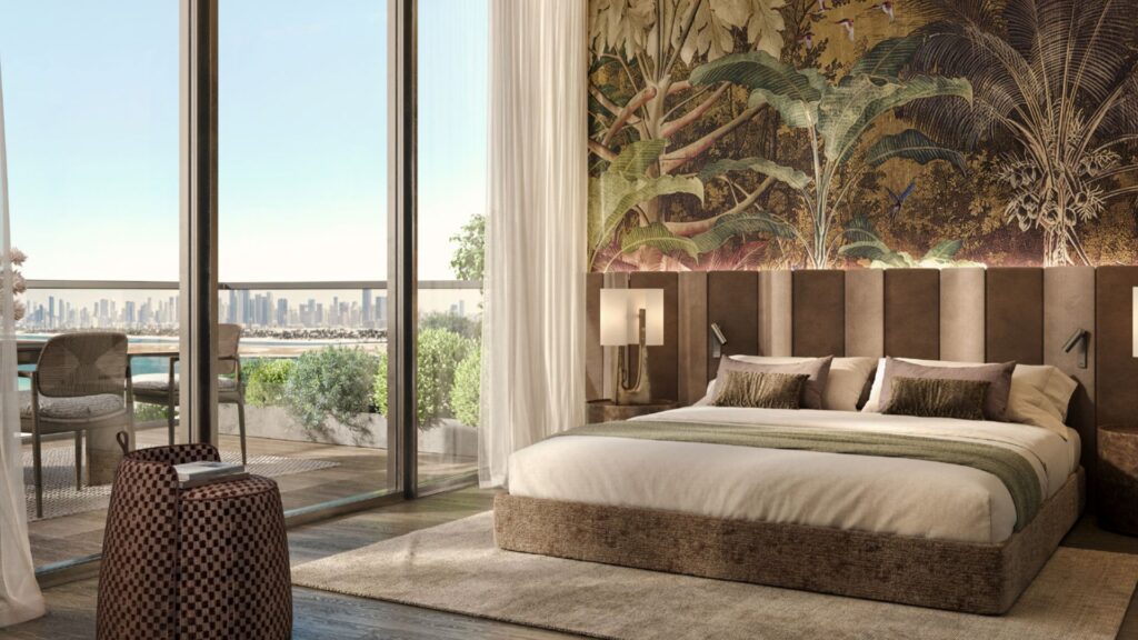 A luxurious room at the Cheval Residences featuring a king-size bed, a tropical accent wall, floor-to-ceiling windows, and a balcony overlooking the city skyline. Sunlight floods the room, highlighting the elegance of the decor and the lush greenery outside.