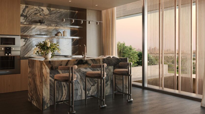 The modern kitchen at Cheval Residences features a large marble island, three bar stools, built-in appliances, and open shelving. Floor-to-ceiling windows with sheer curtains offer picturesque views of the outdoors, complemented by wood accents and natural light.