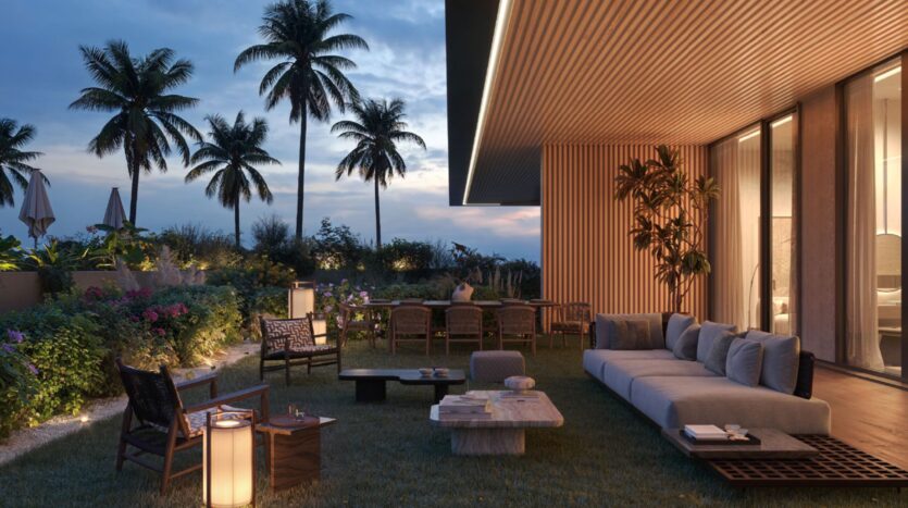 A modern outdoor patio at dusk, featuring comfortable seating, wooden furniture, and warm lighting. Palm trees and lush greenery surround the Cheval residences, creating a tranquil tropical atmosphere.