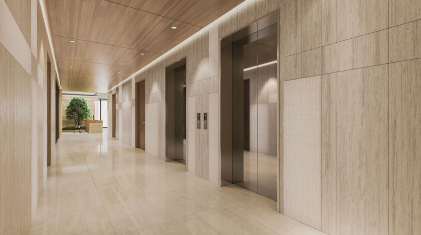 A modern hallway in Derby Heights features light wood walls, polished tile floors, and three stainless steel elevator doors. A potted green plant adds a touch of nature at the end of the hallway.