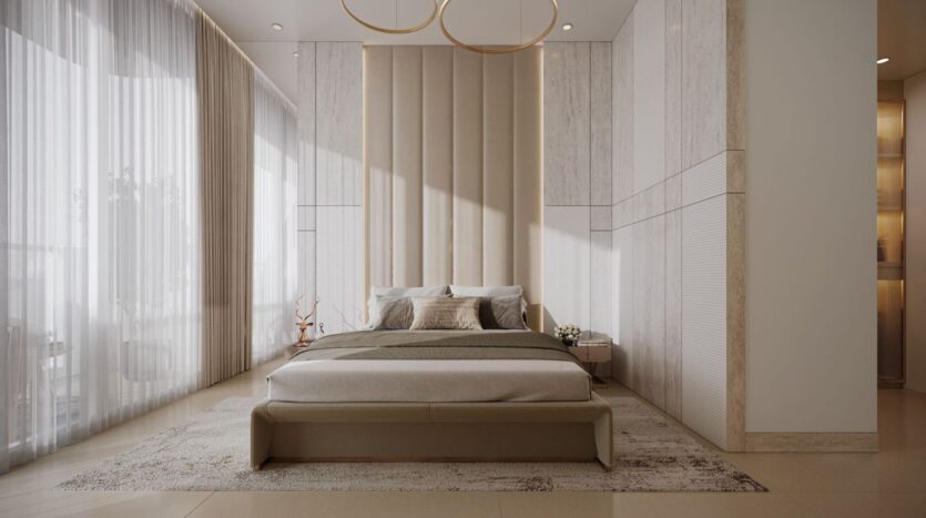A modern, minimalist bedroom in Derby Heights featuring a beige tufted bed, a large upholstered headboard, neutral bedding, and two nightstands. Sheer curtains drape the tall windows, flooding the room with natural light.