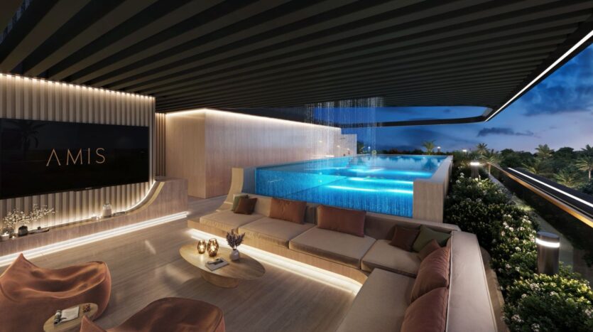 A modern rooftop lounge at dusk, featuring a large, illuminated infinity pool. Derby Heights offers comfortable seating, a stylish coffee table, lush greenery, elegant lighting, and a sign reading "FRIENDS" on the wall.