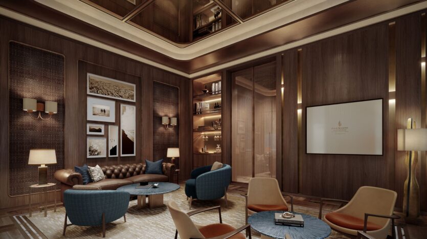 The luxurious living room at Four Seasons Private Residences features wood-paneled walls, modern sofas and chairs, round tables, warm lighting, framed artwork, a wall-mounted screen, built-in shelves displaying decorative items, and a high ceiling with recessed lighting.