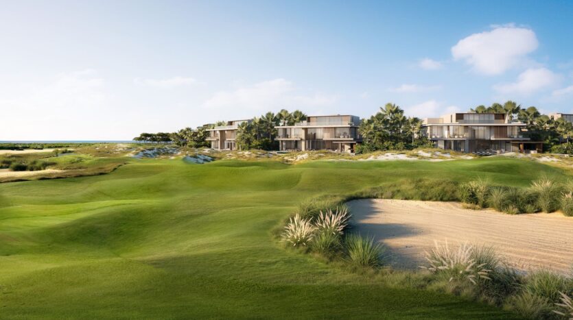 The modern villas at Four Seasons Private Residences are surrounded by palm trees and overlook a lush golf course with manicured greens and a sand bunker, beneath a bright blue sky dotted with scattered clouds.