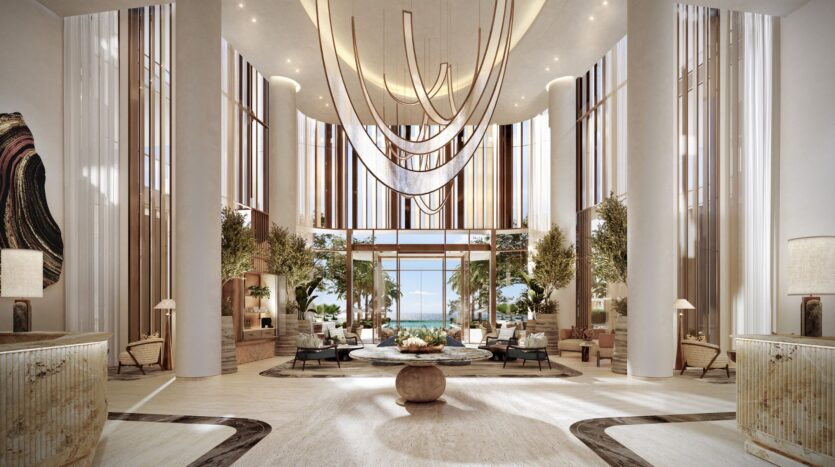 The luxurious lobby of the Four Seasons Private Residences features high ceilings, modern pendant lights, tall columns, large windows with wood accents, indoor plants, elegant seating, and breathtaking ocean views.
