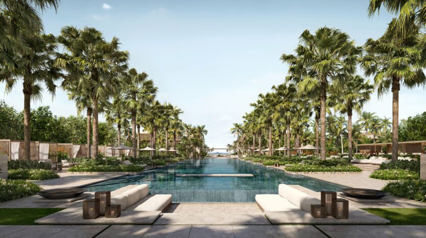 The luxurious Four Seasons private residences feature an outdoor pool lined with palm trees and lounge chairs, leading down to the ocean; elegant landscaping and a clear blue sky create the serene atmosphere of a tropical beach resort.