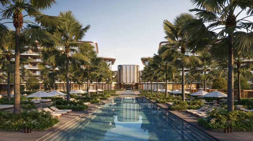 The luxurious outdoor pool at Four Seasons Private Residences, surrounded by palm trees, lounge chairs, and umbrellas, with modern buildings in the background, under a clear sky.