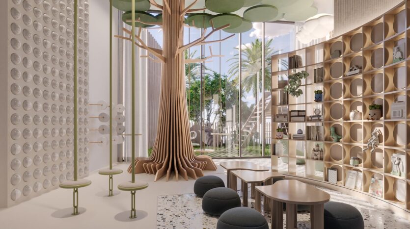 The modern, airy game room at Four Seasons Private Residences features a large wooden tree sculpture, round tables and stools, circular shelves, and large windows overlooking a palm-lined garden. The decor is light, playful, and inspired by nature.