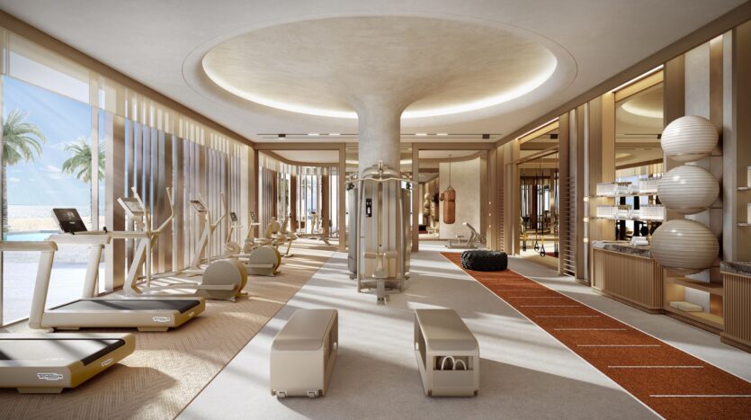 The modern, sun-filled fitness center at Four Seasons Private Residences is equipped with treadmills, exercise machines, benches, fitness equipment, large windows, a running track, mirrored walls, and views of palm trees. The space features neutral colors and a minimalist design.
